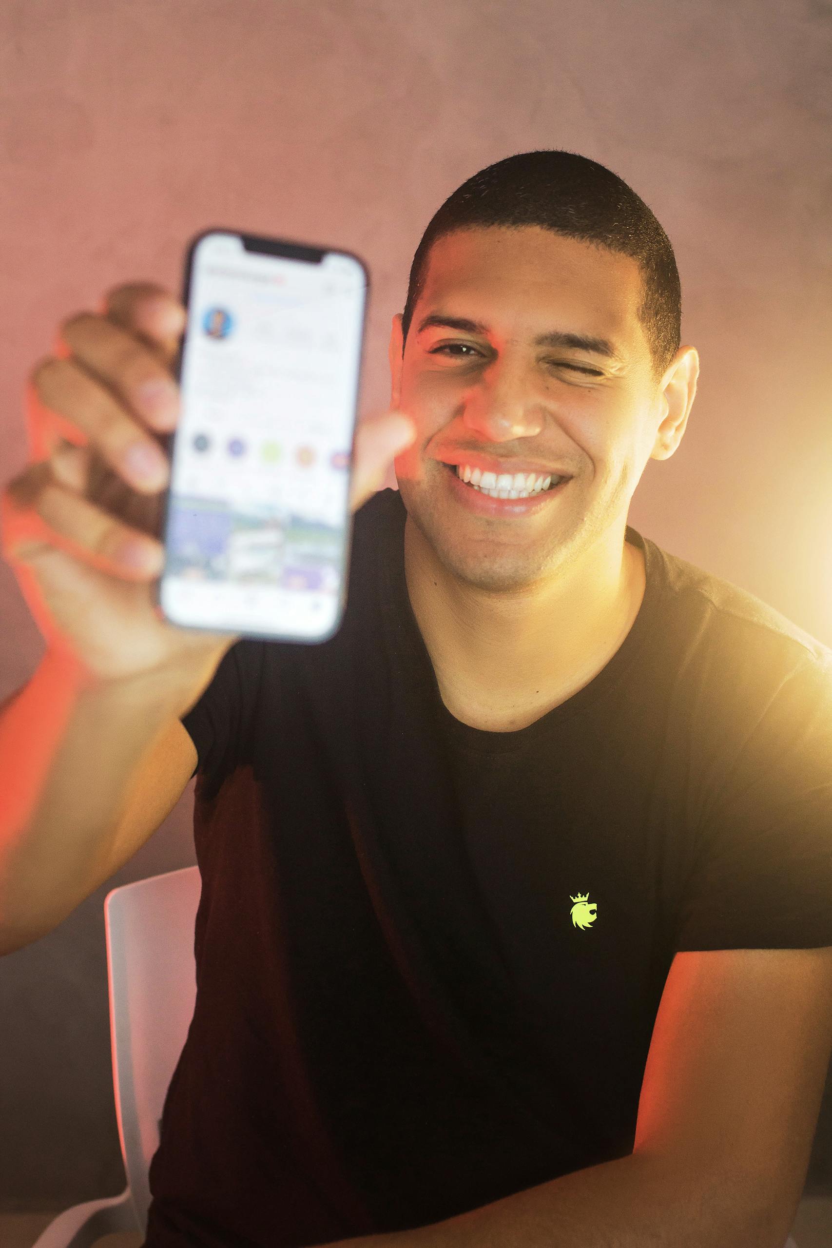 MiaiD Business / Investitori 2 Happy man in a black shirt using a smartphone indoors, smiling and winking.